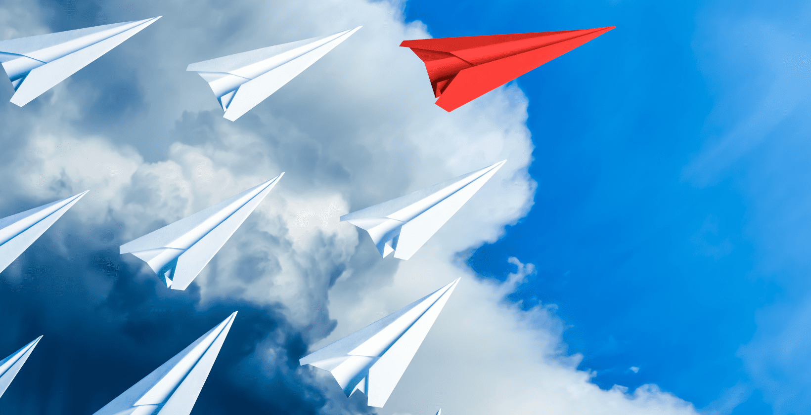 red paper airplane flies ahead of white paper airplanes in the sky