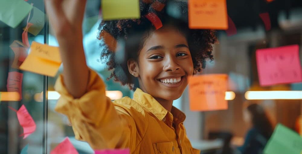 A smiling child is engaging with colorful sticky notes on a window.