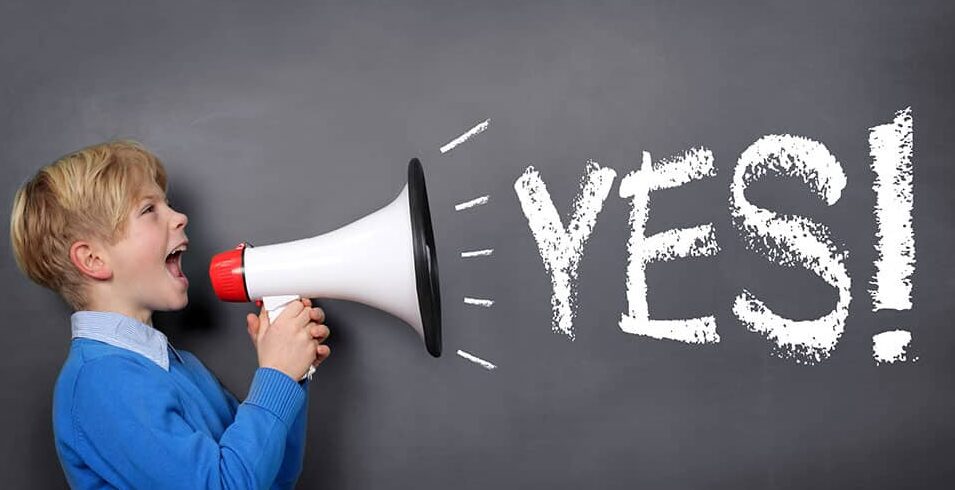 Boy holding megaphone yells YES on grey background